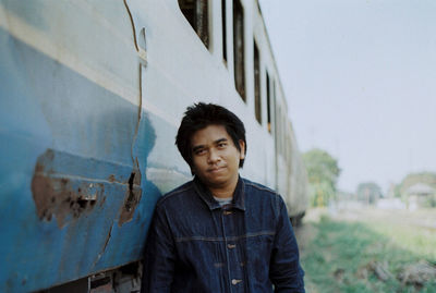 Portrait of young man standing by old weathered train