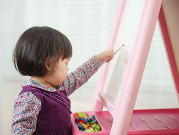 Cute girl writing in whiteboard at home