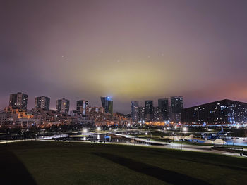 Illuminated modern buildings in city against sky at night