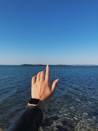 Cropped hand of woman gesturing at beach against clear blue sky