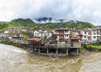 Houses on river by buildings against sky