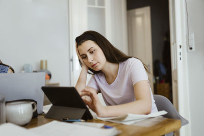 Bored young woman using digital tablet while studying at table