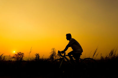 Silhouette man cycling on field against sky during sunset