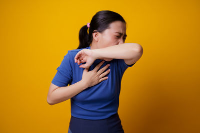 Mid adult woman standing against yellow background
