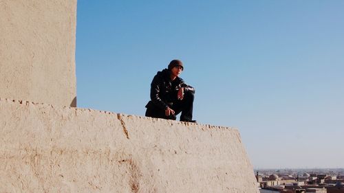 Man looking at view while standing by wall of historic building against clear sky