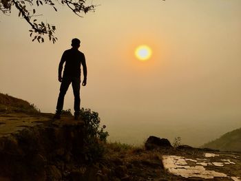 Silhouette man standing on rock against sky during sunset