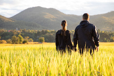 Rear view of couple standing at farm against mountains