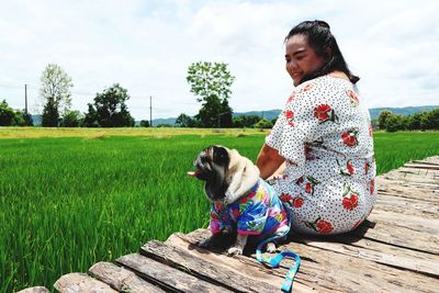 Smiling woman with dog sitting on boardwalk by paddy field 