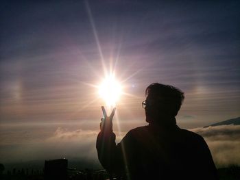 Silhouette man holding sun against sky during sunset