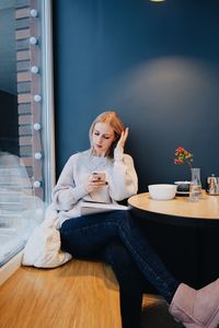 Young woman using phone while sitting on table