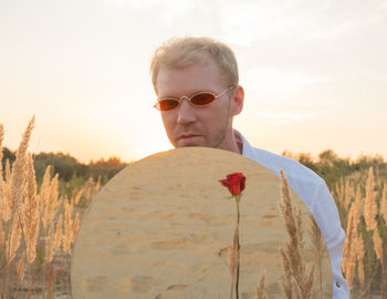 Portrait of young man standing on field against sky