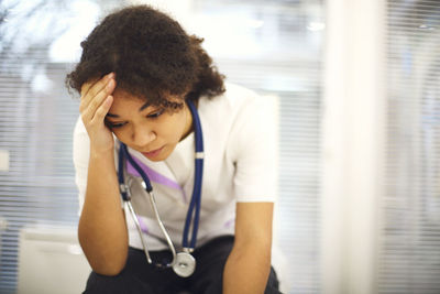 Side view of young woman holding stethoscope at home