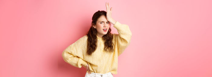 Portrait of young woman standing against yellow background