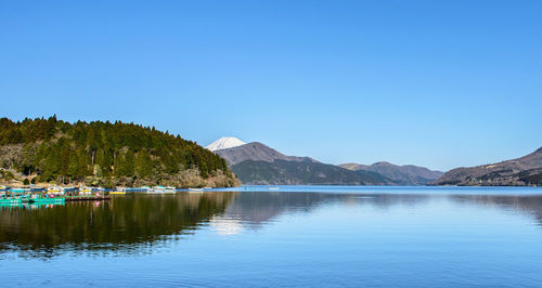 Scenic view of lake and mountains against clear blue sky