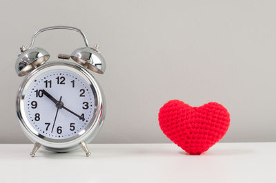 Close-up of heart shape clock on table against white background