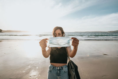 Portrait of young woman standing at beach against sky