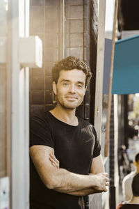 Smiling male owner with arms crossed leaning on doorway