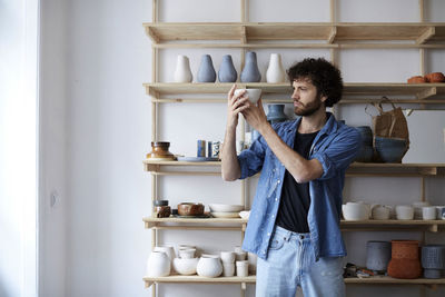 Young man holding camera while standing in shelf