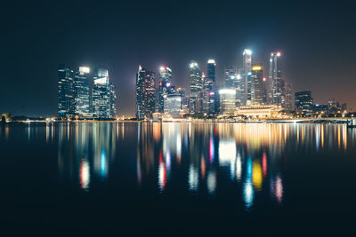 Illuminated buildings by river against sky at night