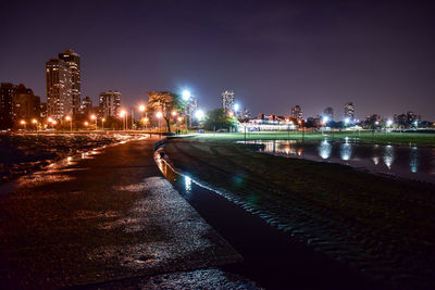 Illuminated city by river against sky at night