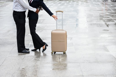 Low section of couple standing by luggage on footpath