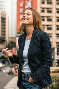 Smiling young woman standing against buildings in city