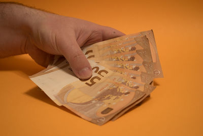 Close-up of hand holding paper against orange background