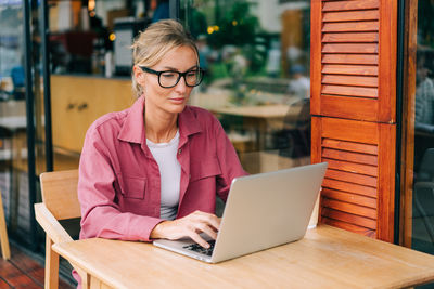 Young blonde business woman sitting on the terrace in a cafe working on a laptop.