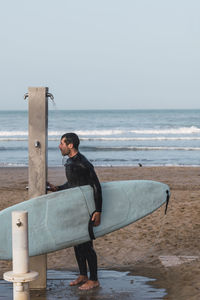 Full length of man with surfboard on beach against sky