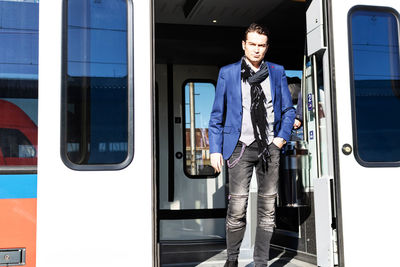 Businessman getting out of subway train while commuting to work and looking at camera.