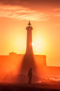 Silhouette of man standing by lighthouse against sky during sunset