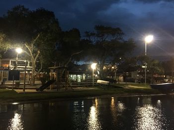 Illuminated street by canal in city at night