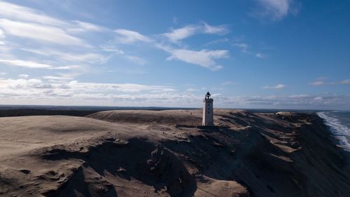 Lighthouse on beach by sea against sky