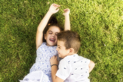 High angle view of happy siblings lying on grassy field at park