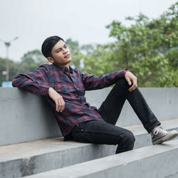 Young man looking away while sitting on railing