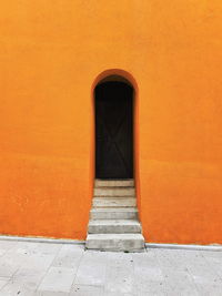 Architectural minimalism, orange wall, stairs and dark door.