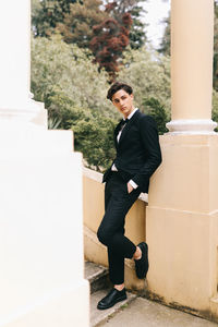 A beautiful young man, the groom in an elegant wedding suit, stands posing in the city's old park