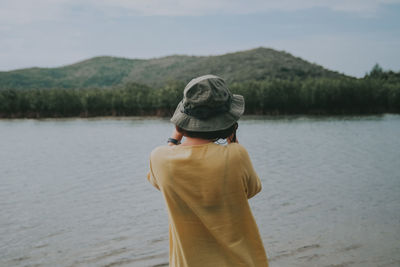 Rear view of man standing by lake against sky