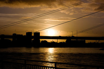 Silhouette of bridge over river during sunset