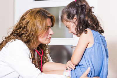 Female doctor looking at girl suffering from stomach ache in hospital ward