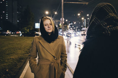 Portrait of woman standing on illuminated street in city at night