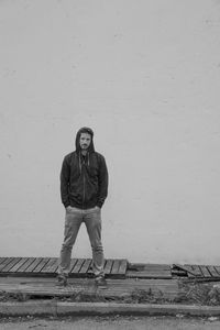 Portrait of young man with hands in pockets standing against wall