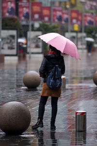 Rear view of woman with umbrella standing in rain