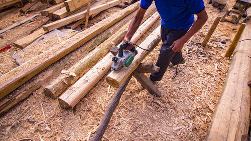 Low section of male worker cutting log with circular saw at construction site