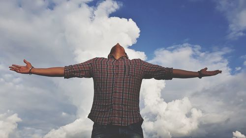 Low angle view of man with arms outstretched standing against cloudy sky