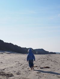 Rear view of girl walking at beach against sky