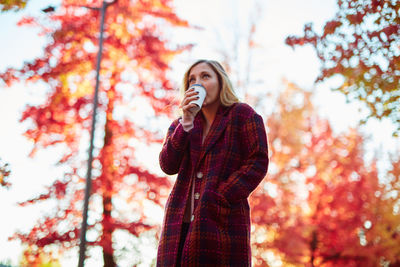 Low angle view of woman standing against sky during autumn
