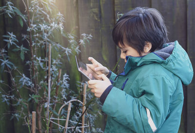 Side view of boy using digital tablet by plants outdoors