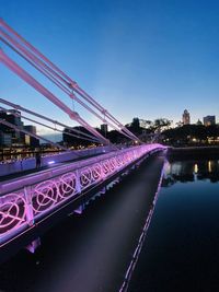 Light trails on bridge over river against sky in city at night