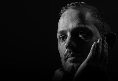 Close-up of thoughtful man with hand on chin against black background